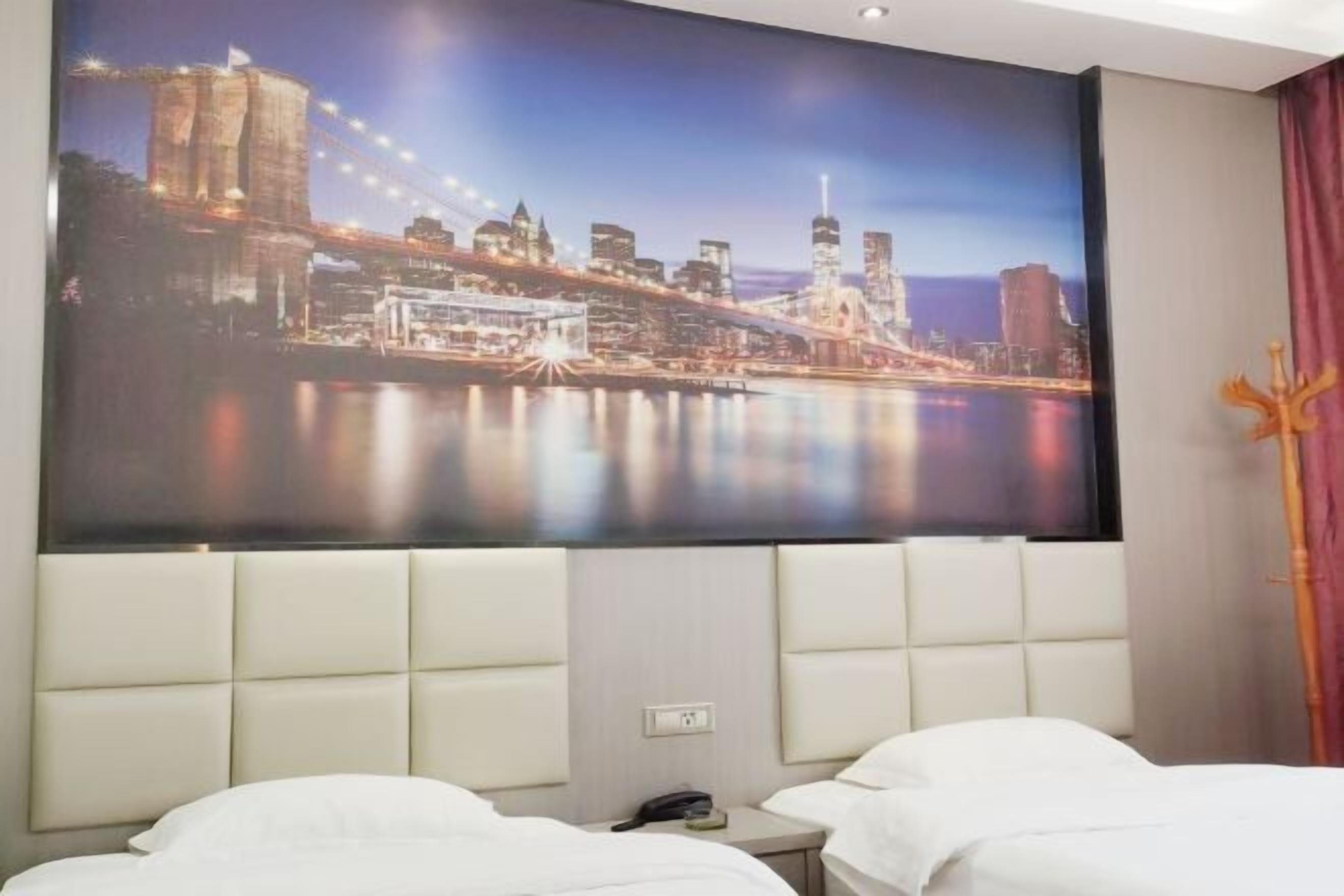 Habitación de hotel con un gran mural de paisaje urbano en la pared, una cama moderna y una mesita de noche con un teléfono.