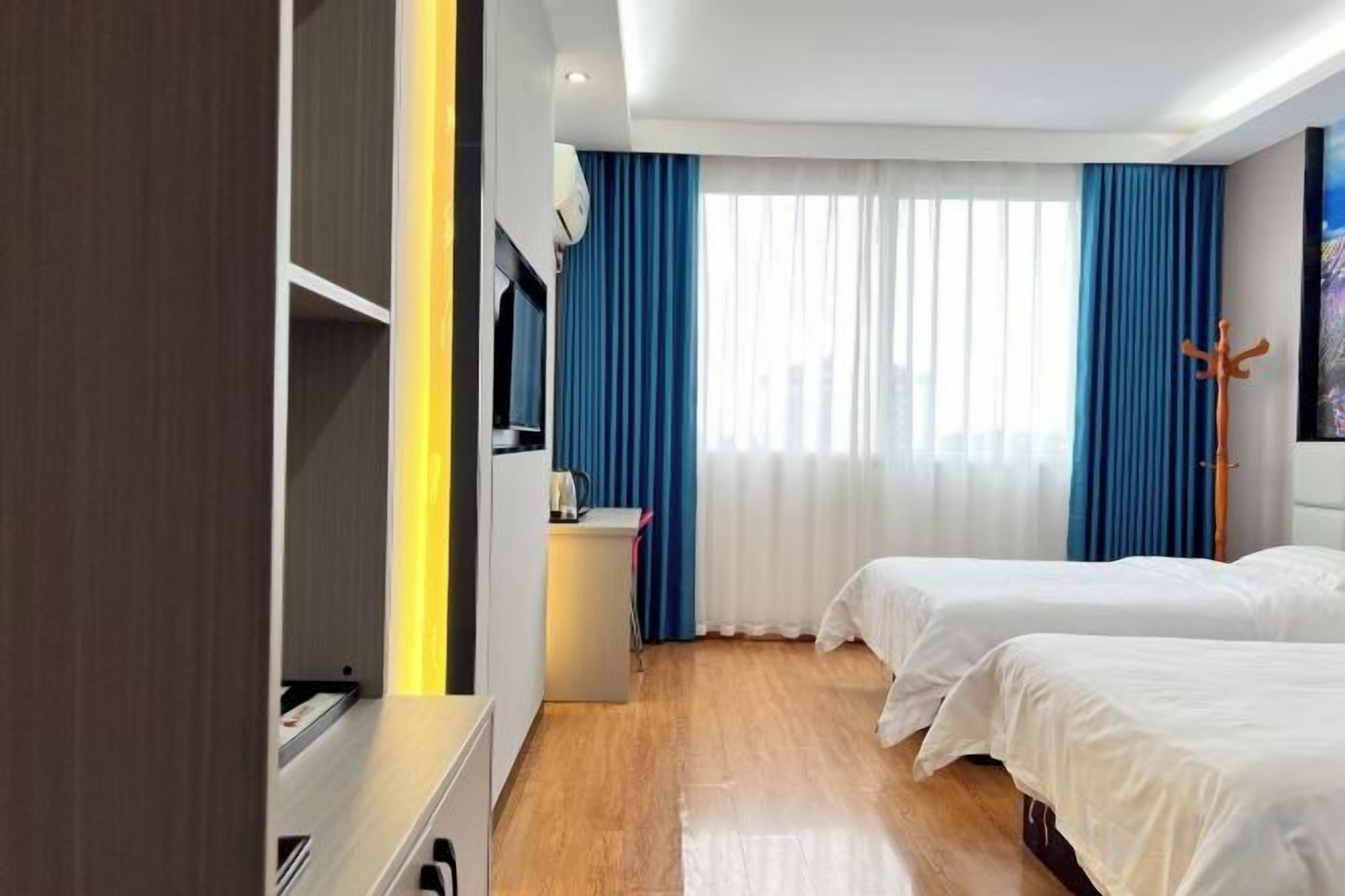 A hotel room with two beds, a desk, a chair, a TV, and a window with curtains.