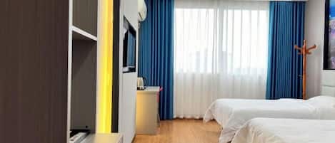 A hotel room with two beds, a desk, a chair, a TV, and a window with curtains.