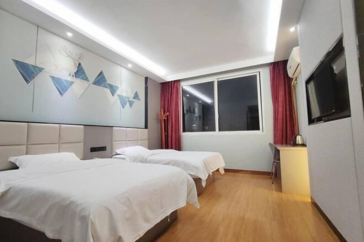 Habitación de hotel con dos camas, un ventanal grande, un televisor y aire acondicionado instalado en la pared.