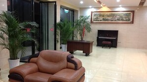 Um saguão com sofá de couro, um piano, plantas em vasos e uma pintura na parede.