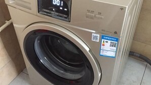 Vista frontal de uma máquina de lavar com visor digital e um adesivo com código QR.
