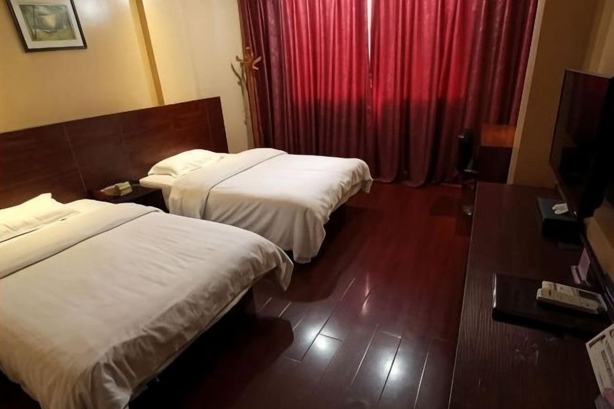 A hotel room with two beds, a wooden headboard, a desk with a chair, and a TV.