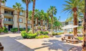 Relax by the pool surrounded by lush greenery and palm trees, with a covered seating area and tables nearby.