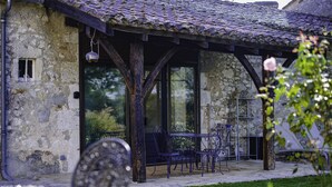 Ein Steinhaus mit einem Ziegeldach, einer überdachten Terrasse mit Sitzgelegenheiten und einer Rasenfläche.