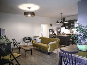 A modern kitchen with a central island, a dining area with a wooden table and chairs, and a living area with a sofa and chairs.