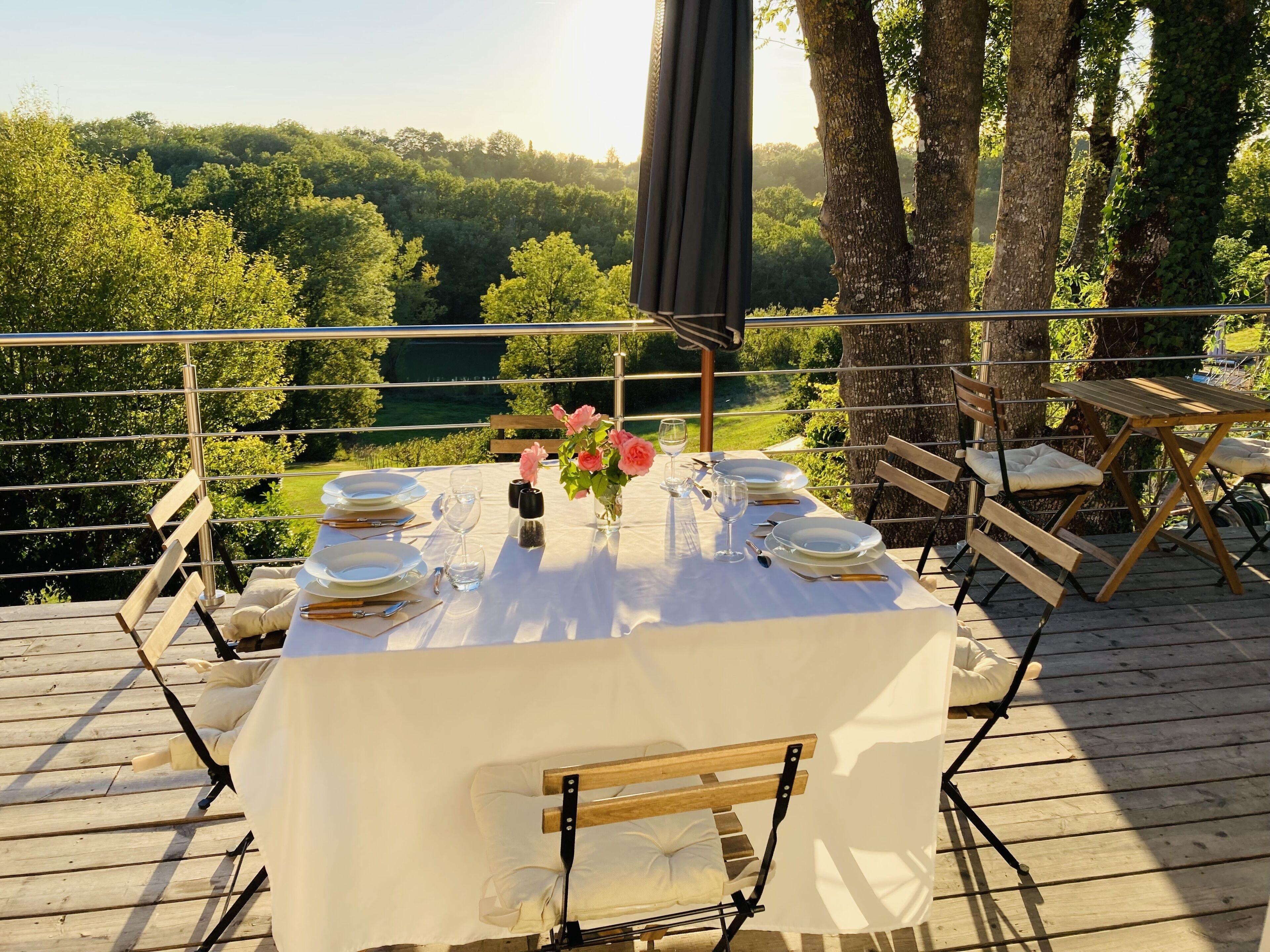 Un espace de restauration en plein air avec une table dressée pour quatre personnes, entourée de chaises en bois, offrant une vue sur un paysage verdoyant et luxuriant.