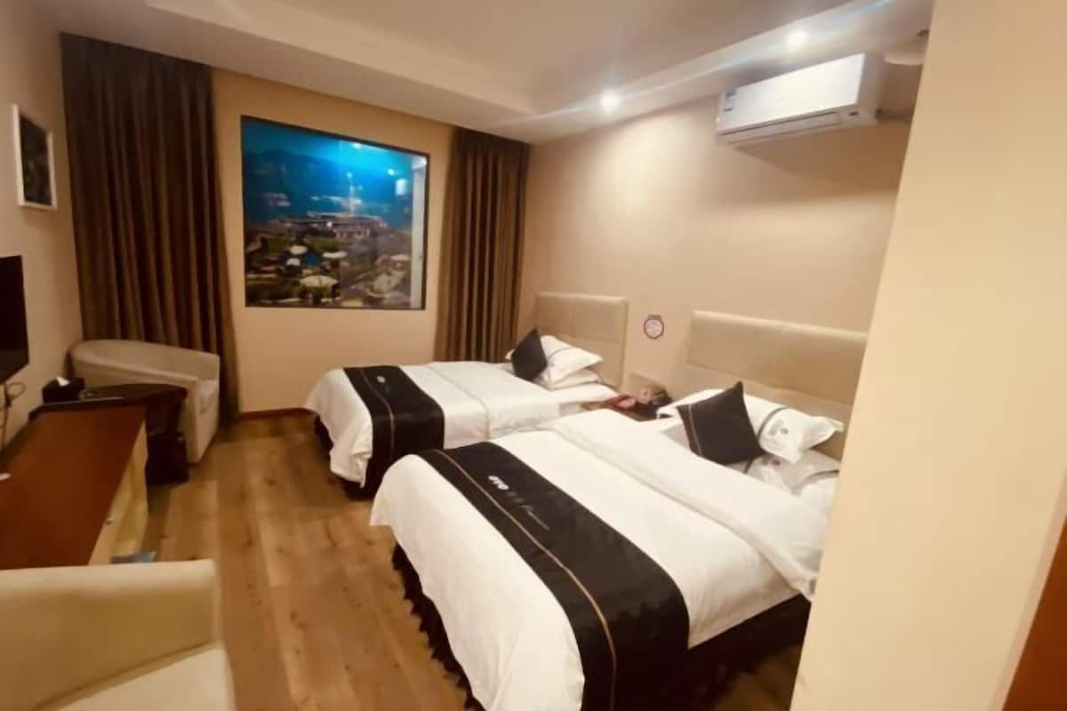 A hotel room with two beds, a desk, a chair, a TV, and a large window with a cityscape view.