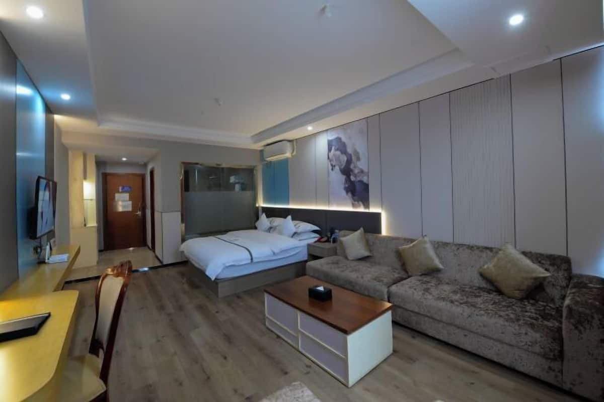 A modern hotel room with a bed, a sofa, a TV, and a desk.