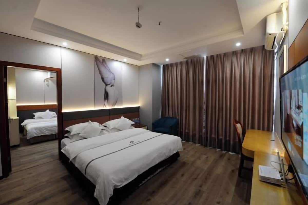 A hotel room with a large bed, a desk with a computer, a chair, a TV, and a window with curtains.
