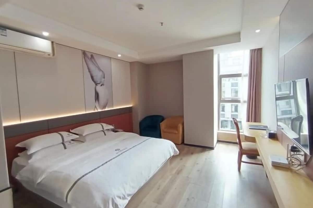 A hotel room with a bed, a desk with a computer, a chair, and a large window.