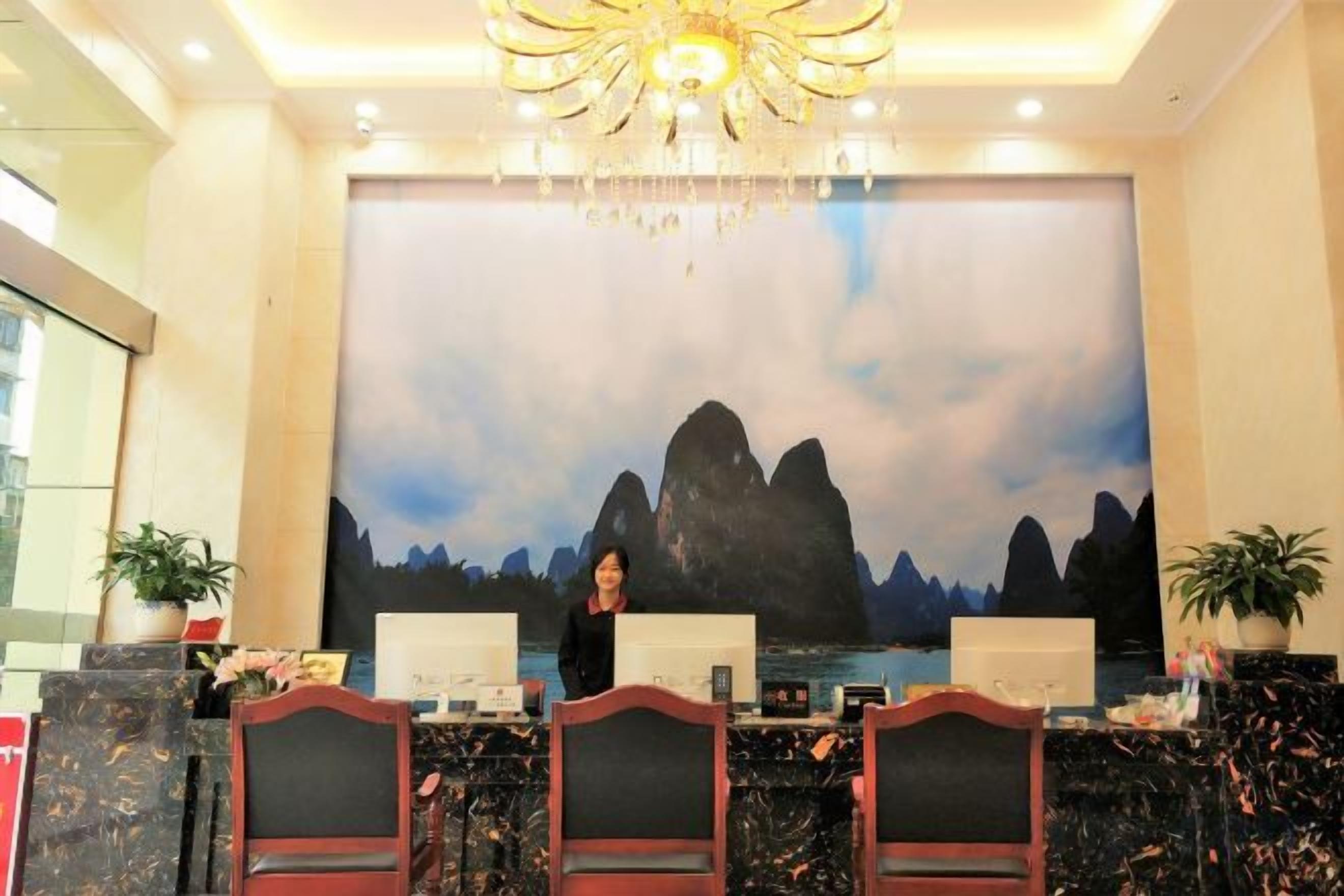 A reception desk with a large painting of mountains in the background, a chandelier, and a modern design.