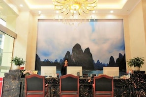 A reception desk with a large painting of mountains in the background, a chandelier, and a modern design. - Hongye Holiday Hotel (Shuifu)