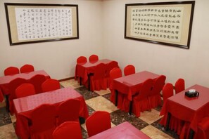 A conference room with red tables and chairs, framed calligraphy on the walls, and a checkered floor. - Hongye Holiday Hotel (Shuifu)