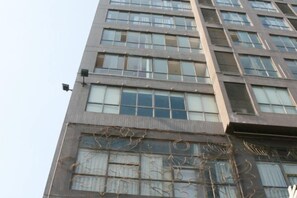 A multi-story building with a modern architectural design, featuring a series of windows and a visible security camera. - Hongye Holiday Hotel (Shuifu)