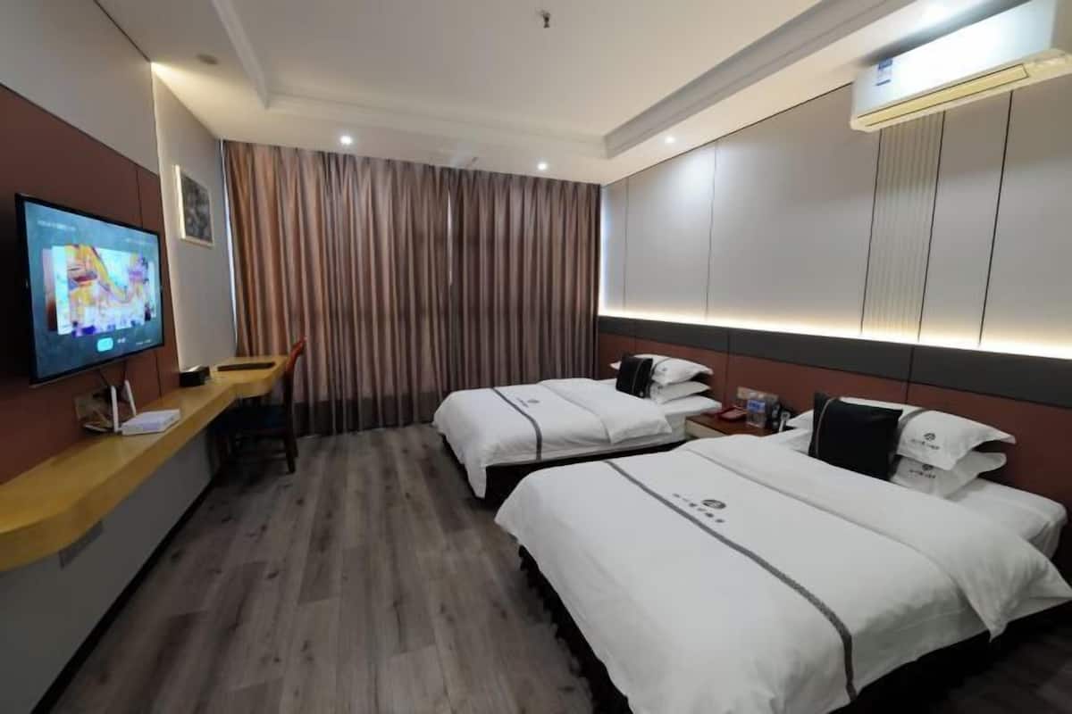 A hotel room with two beds, a desk with a flat-screen TV, a wall-mounted air conditioner, and a curtain backdrop.