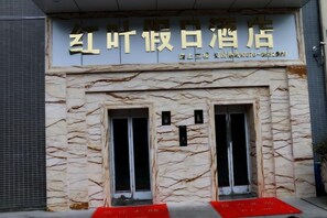 A building facade with a sign indicating a restaurant or cafe. There are two visible windows with black frames and a red mat at the entrance. - Hongye Holiday Hotel (Shuifu)