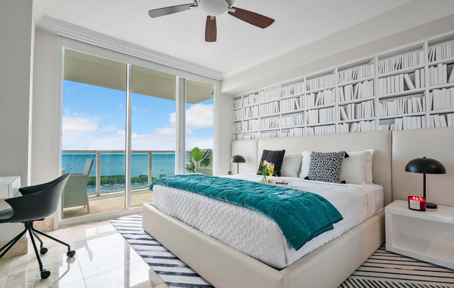 Un dormitorio con una cama grande, una estantería, un escritorio y vista al mar.