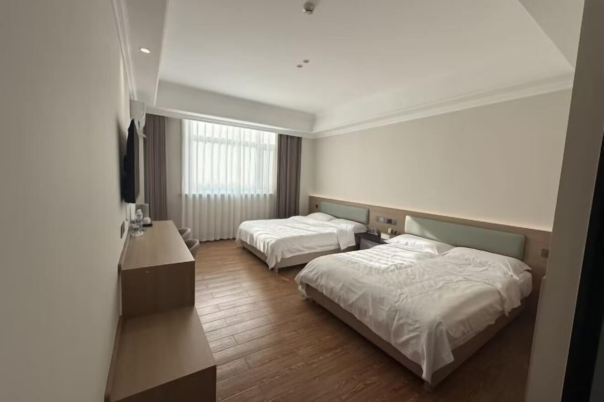 A hotel room with two beds, a desk, a TV, and a large window with curtains.