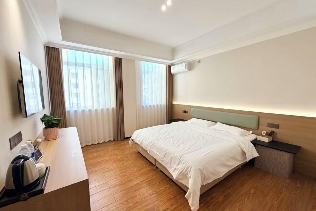 A hotel room with a bed, bedside table, TV, and a desk with a chair.