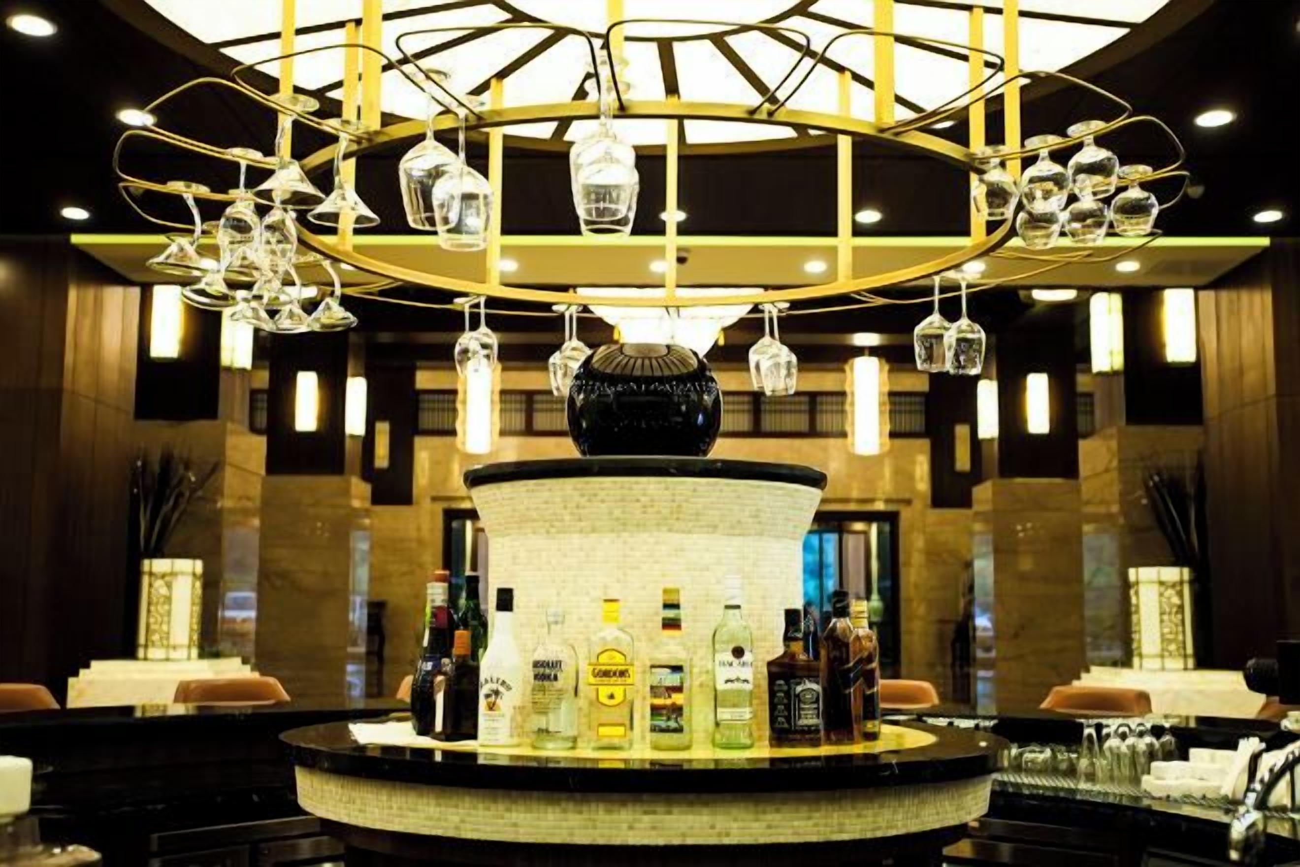 A bar area with a central round bar, multiple hanging light fixtures, and a variety of bottles on the bar counter.