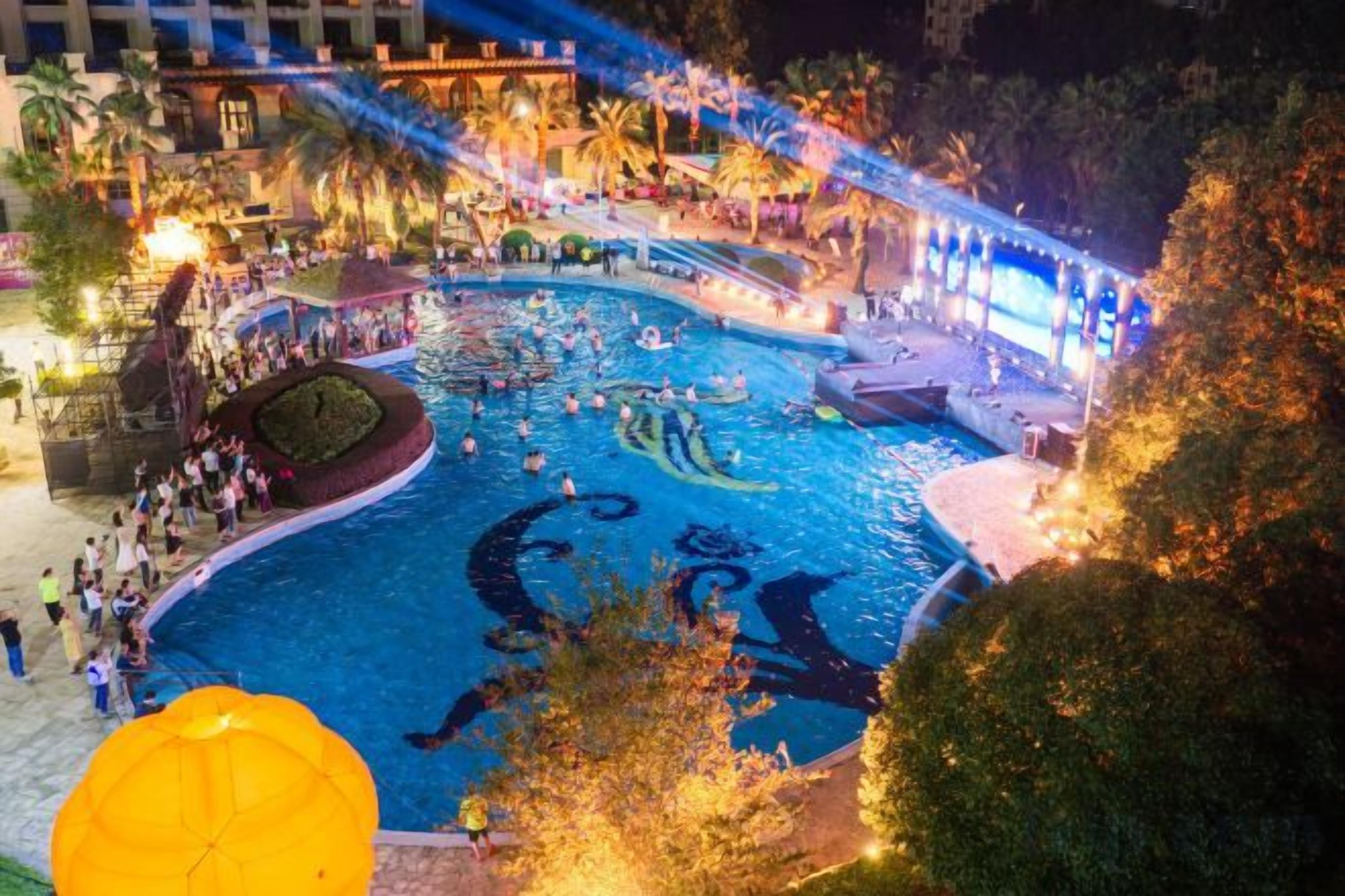 A swimming pool area with a fountain, surrounded by trees and a covered walkway.