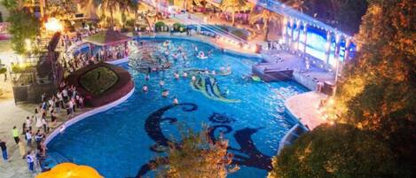 A swimming pool area with a fountain, surrounded by trees and a covered walkway.