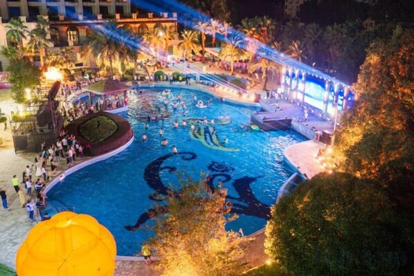 A swimming pool area with a fountain, surrounded by trees and a covered walkway. - Yichun Grand Metropark Resort (Yichun)