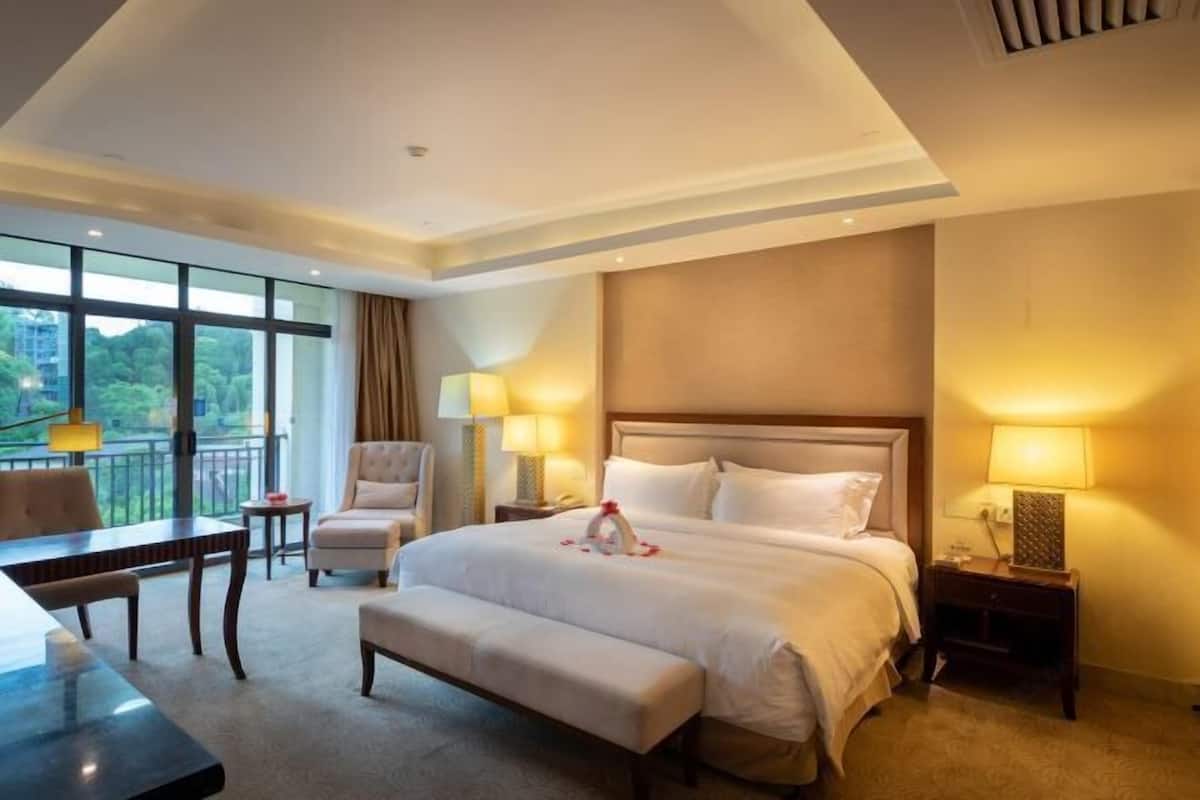 A hotel room with a large bed, a desk, a chair, and a view of the outdoors.