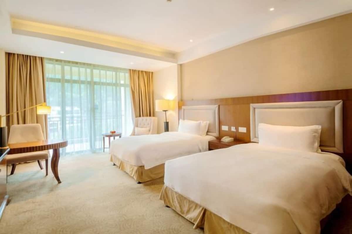 A hotel room with two beds, a desk, a chair, and a large window with curtains.