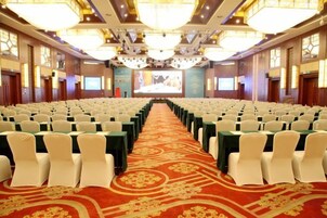 Un salón de conferencias con filas de sillas, piso alfombrado y una pantalla de proyección al frente.
