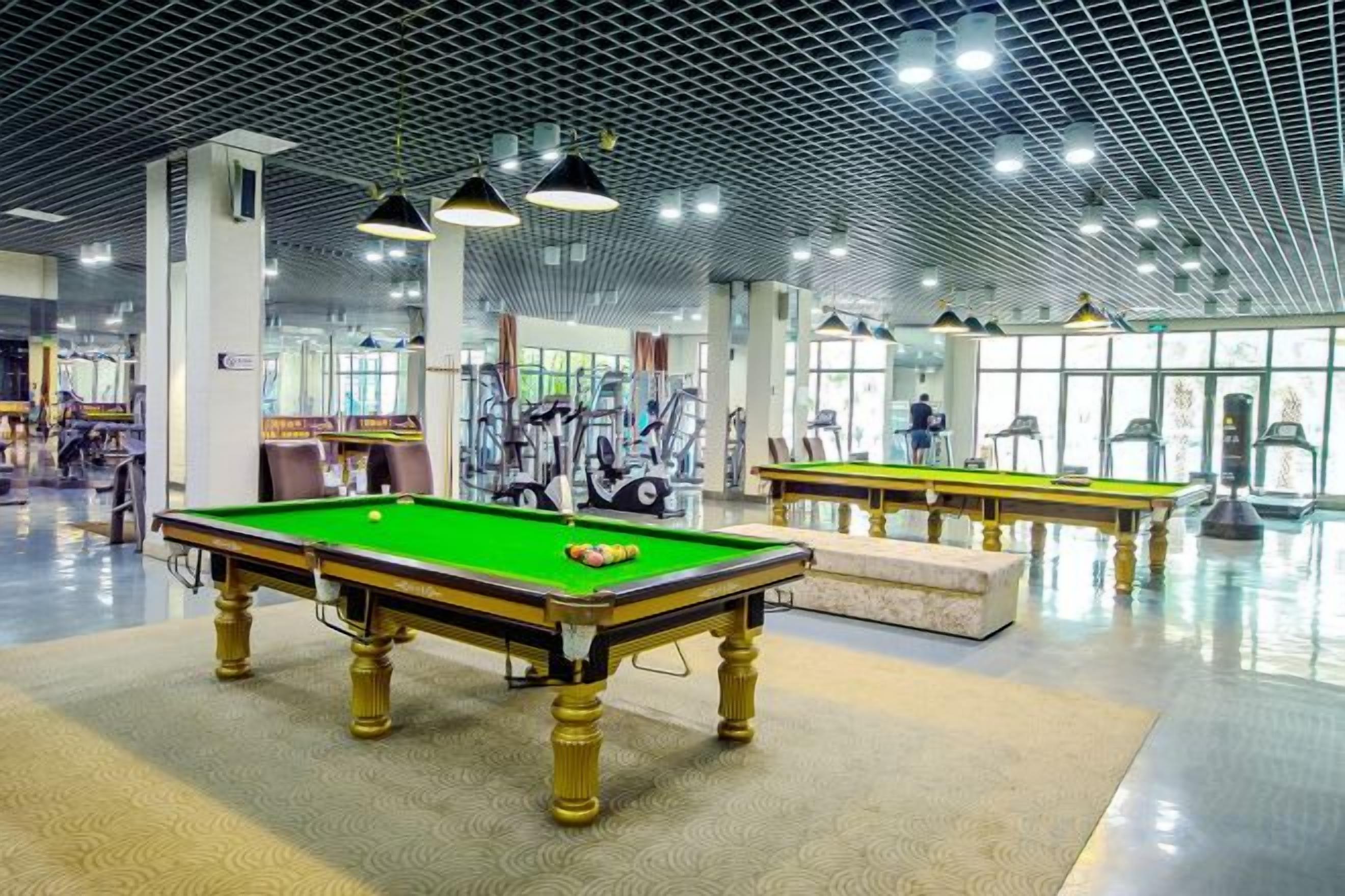 A billiards hall with multiple tables, exercise equipment, and a modern ceiling design.