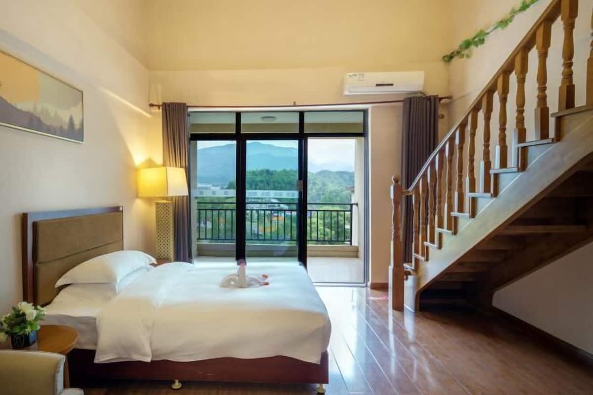 A hotel room with a bed, a nightstand, a lamp, a window with a view of mountains, and a staircase.