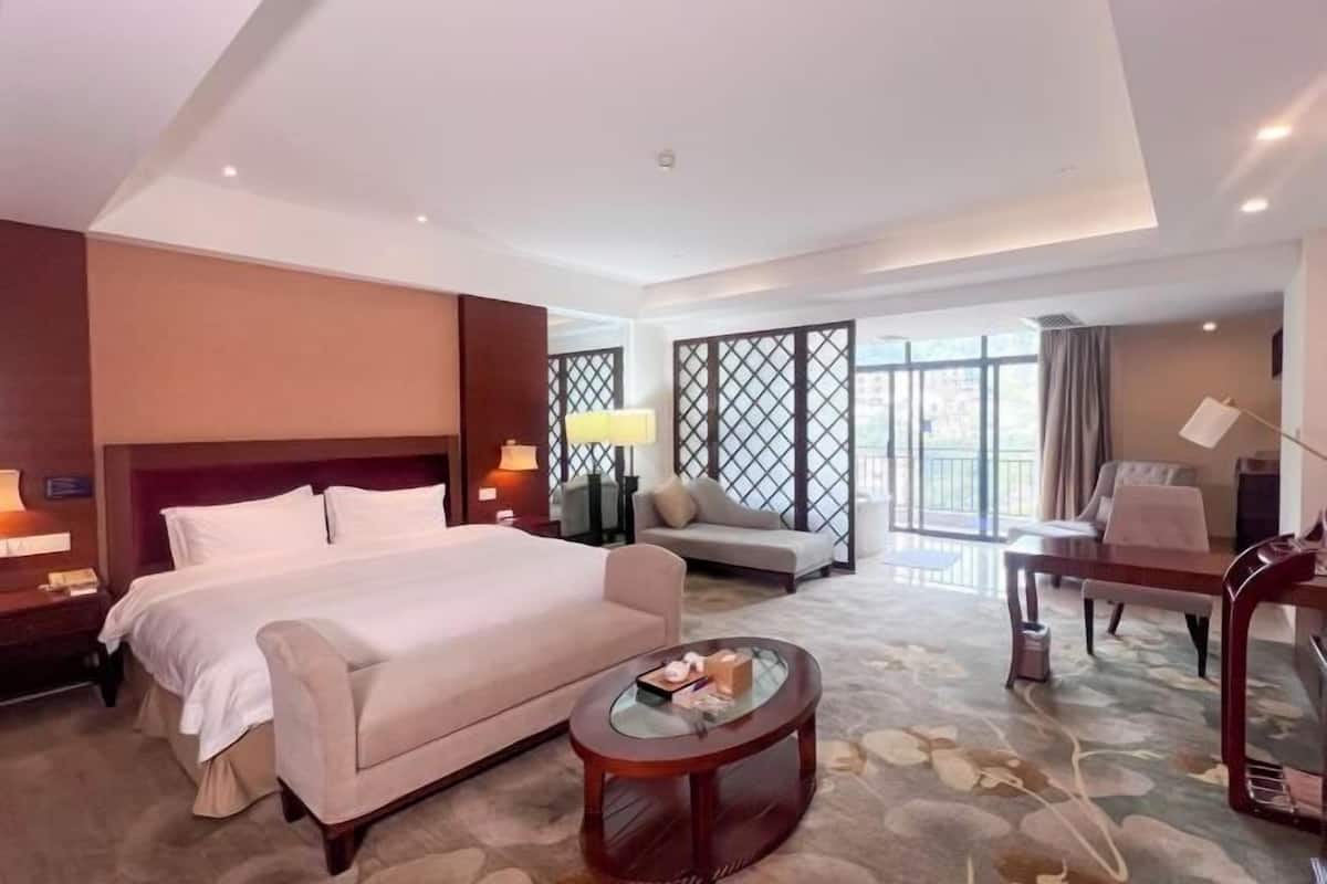 A hotel room with a large bed, a sofa, a small table, and a view of the outdoors.