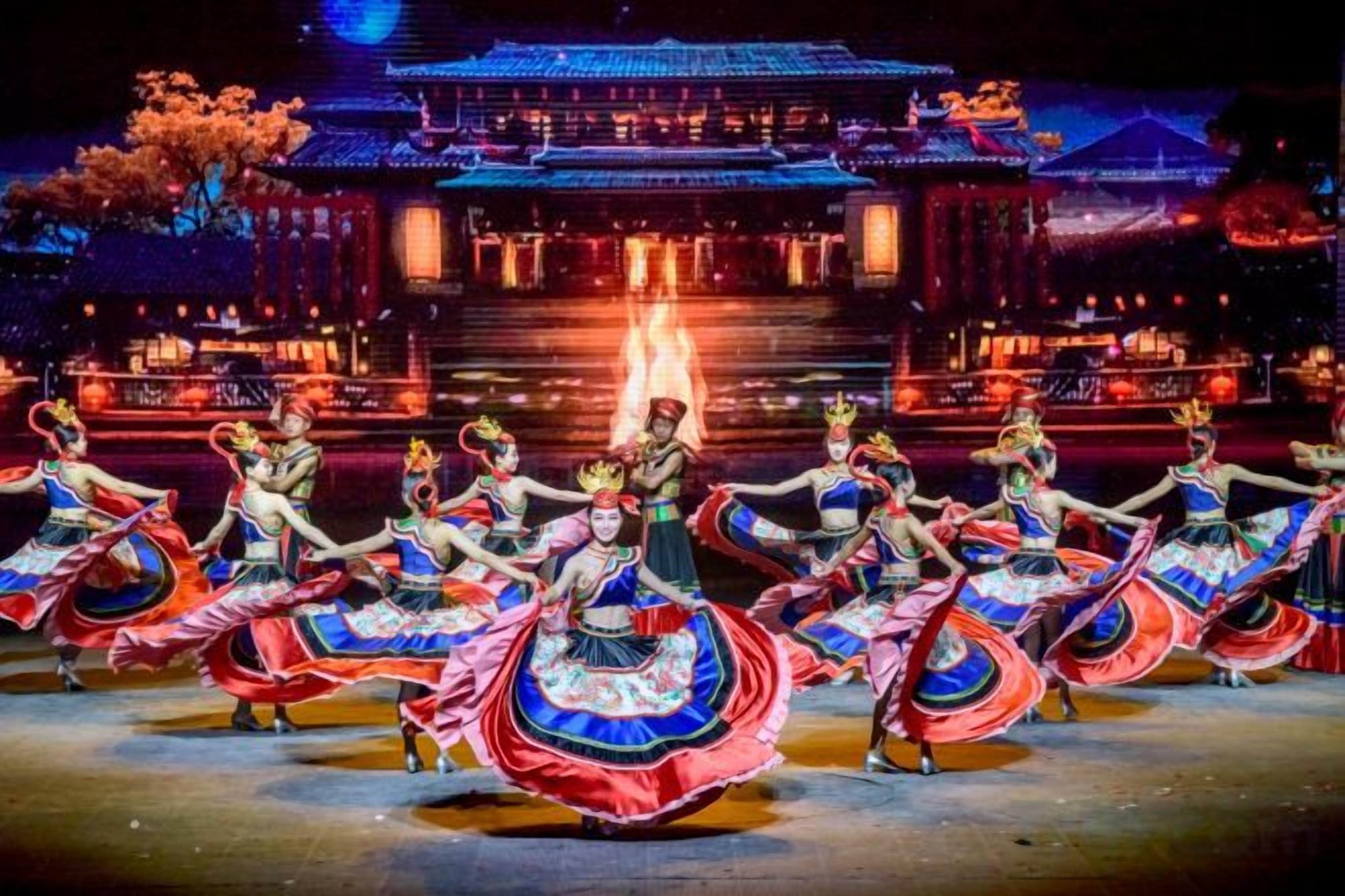 Un groupe de danseurs, vêtus de costumes traditionnels, se produit devant un bâtiment dont les fenêtres sont illuminées.