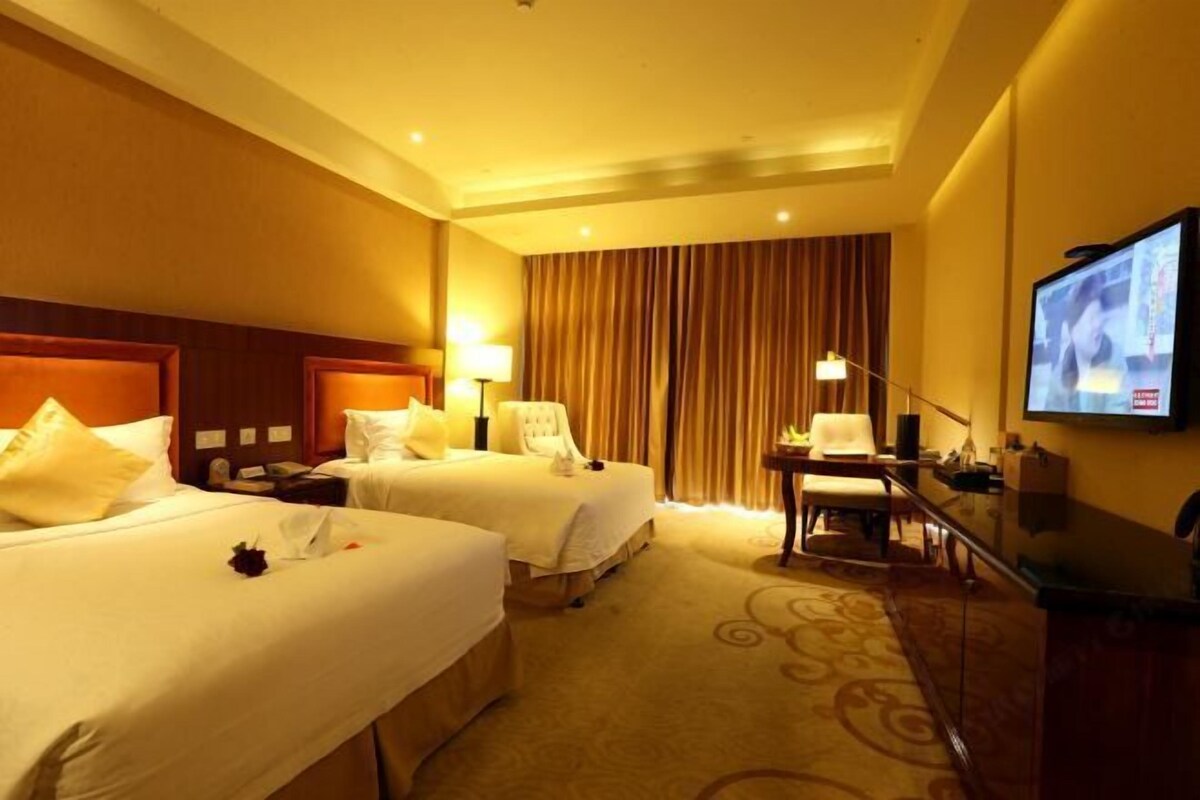 A hotel room with two beds, a television, a desk, and a chair.