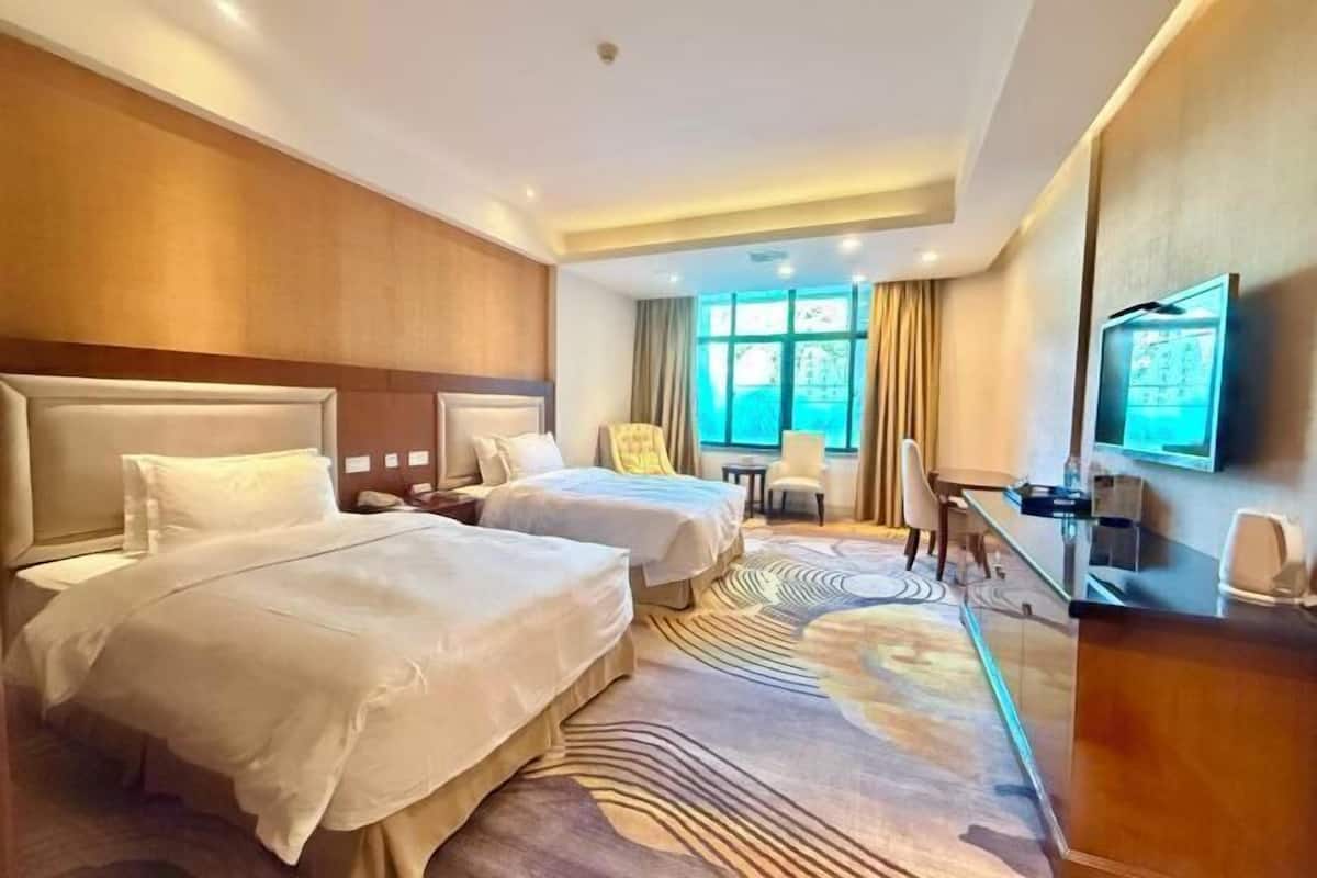 A hotel room with two beds, a desk, a chair, a TV, and a window with curtains.