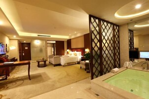 Una habitación de hotel con cama, zona de estar, una mesita, televisor y bañera.