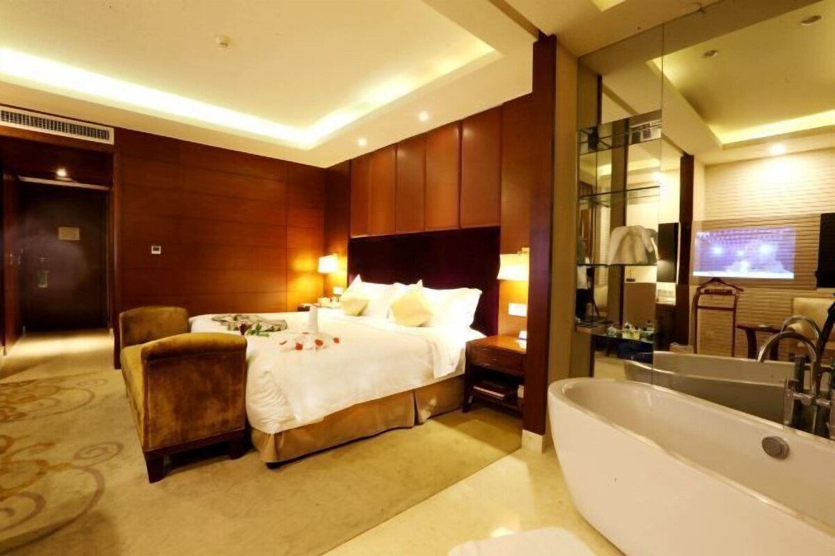 A hotel room with a large bed, a sitting area with a chair, a bathtub, and a mirror.