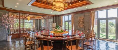A spacious dining area with a round table, multiple chairs, and a large chandelier.