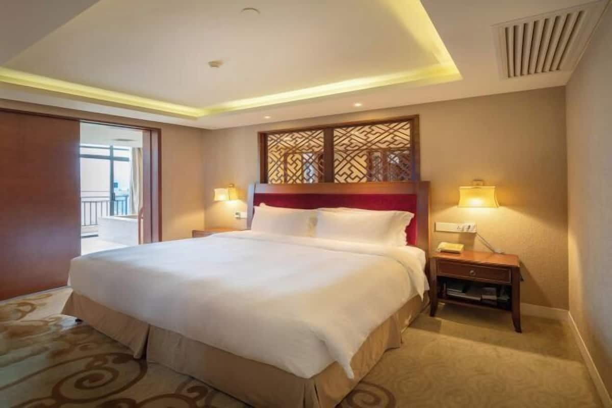 A hotel room with a large bed, two bedside lamps, a small nightstand, and a decorative headboard.