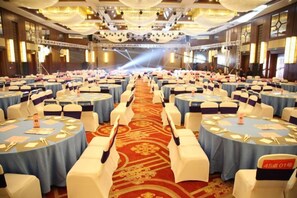 Une grande salle de banquet avec des tables rondes, des chaises blanches et un tapis rouge.