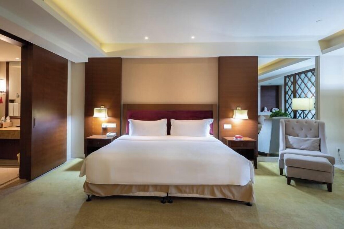 A hotel room with a large bed, two bedside tables, a chair, and a view of the hallway.