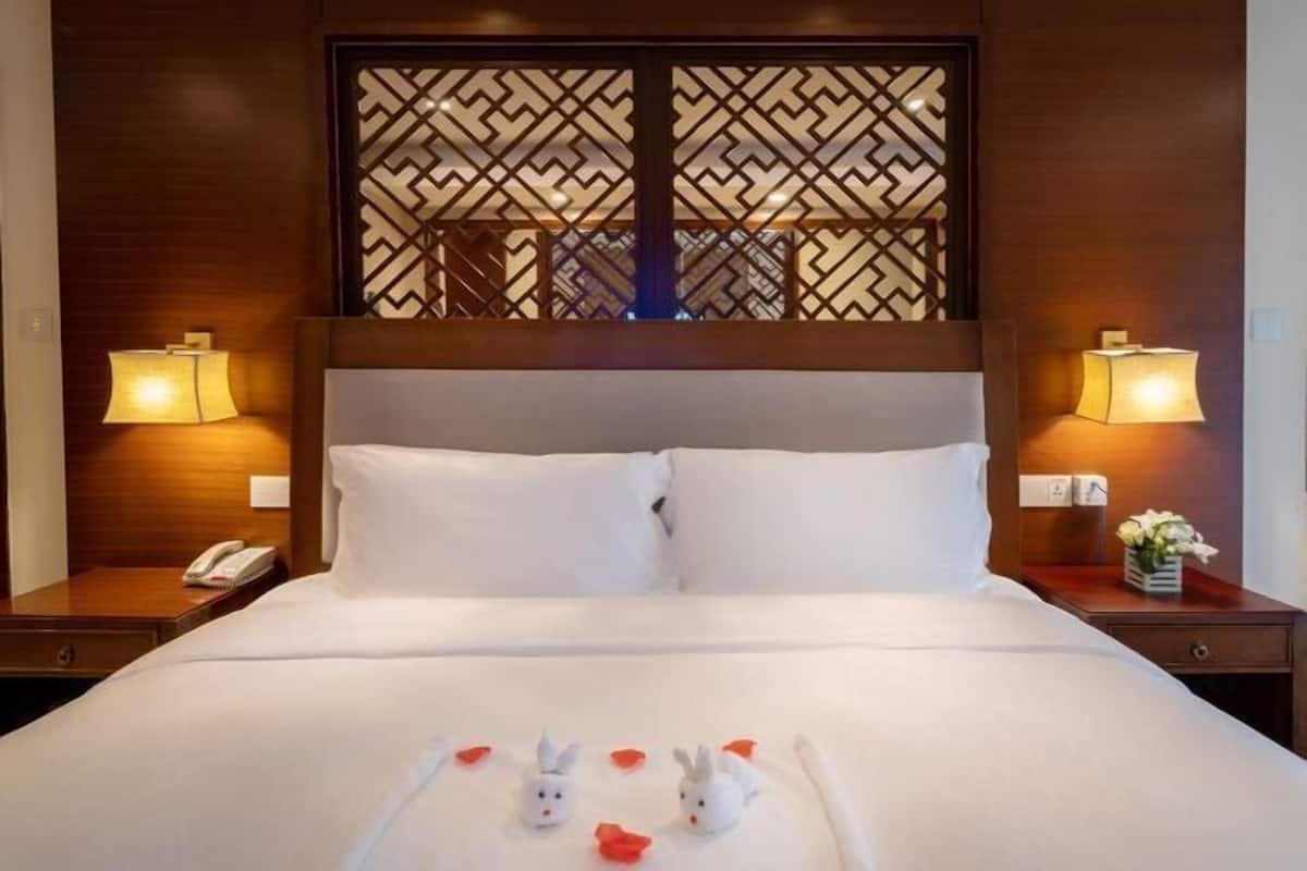 A hotel room with a large bed, two bedside tables with lamps, a decorative screen, and a floral arrangement.