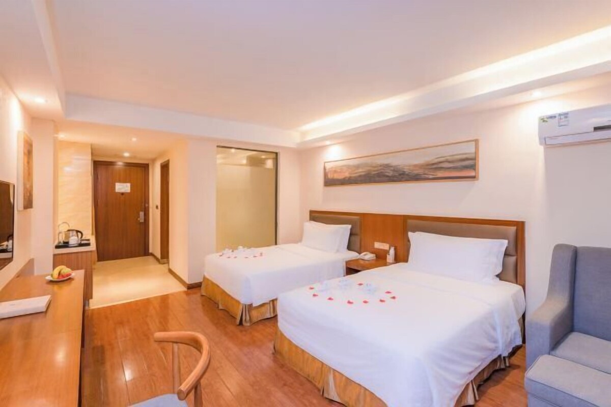 A hotel room with two beds, a desk, a chair, and a TV.