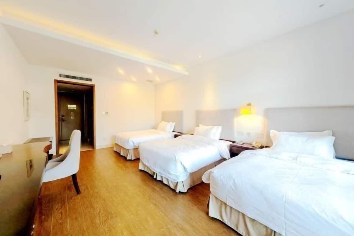 A hotel room with three beds, a desk, and a chair.