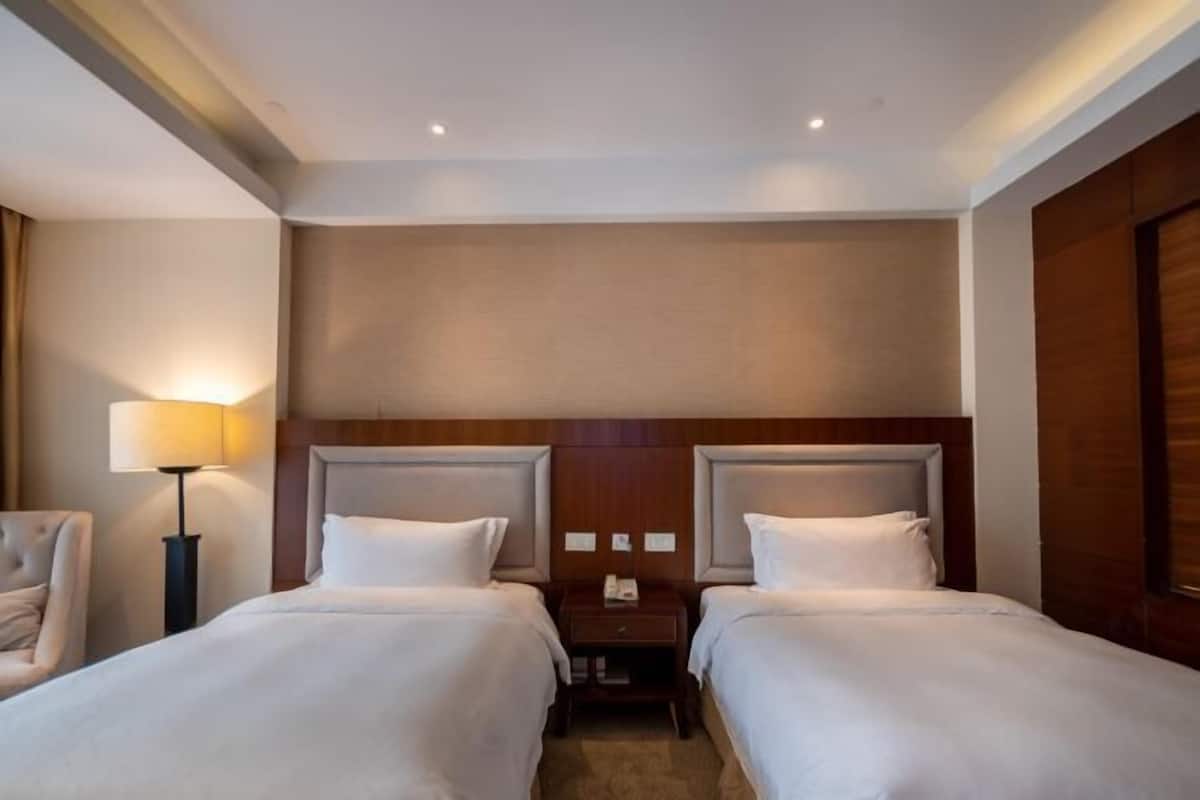 A hotel room with two beds, a nightstand, a lamp, and a wooden headboard.