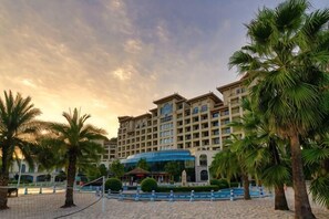 A hotel with a pool, palm trees, and a clear sky.