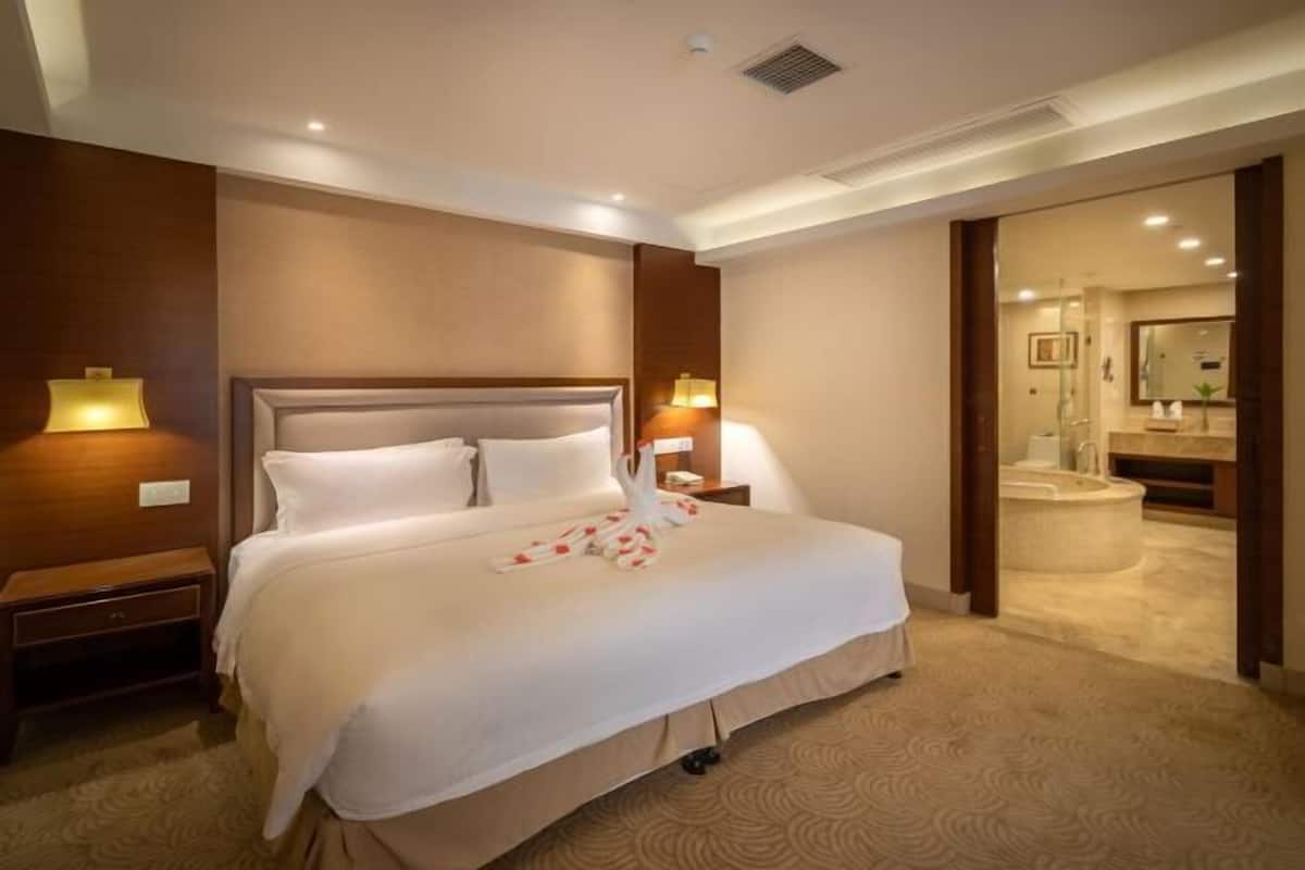 A hotel room with a large bed, bedside lamps, a nightstand, a bathroom with a bathtub, and a mirror.