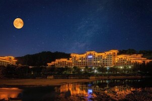 Un hotel de varios pisos, con una extensa masa de agua al frente y una luna llena en el cielo.